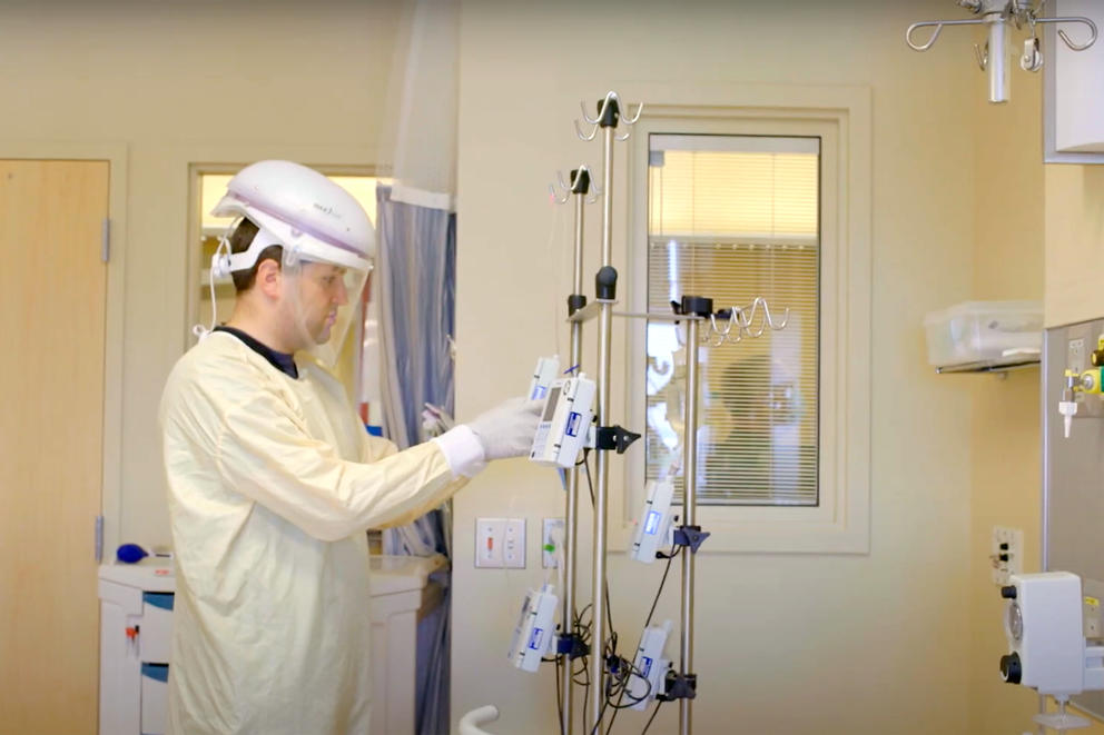 Paul Fuller wears PPE including a gown, gloves and helmet as he manipulates nursing machinery in a hospital room