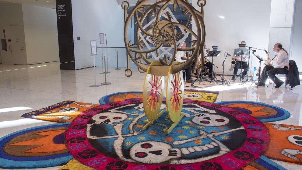 photo of a large colorful sandpainting on the floor of a lobby with musicians playing