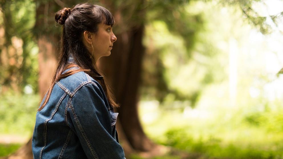 a movie still showing a jean jacketed woman in profile, with long brown hair, looking off into an unfocused green space