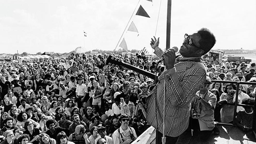 vintage black and white photo of a black singer in sunglasses performing outdoors in front of a huge crowd