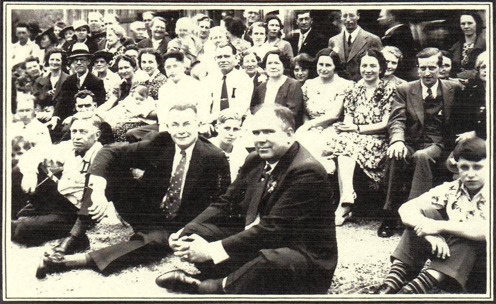 A sepia photo of a group of men sitting in chairs and on the floor