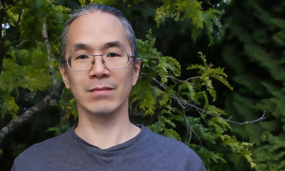 photo of a man wearing glasses and standing outside in front of a tree