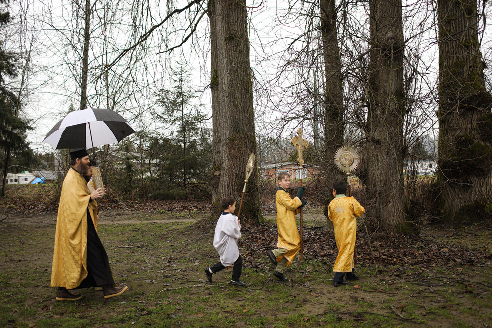 A priest and three altar boys walk through a wooded area