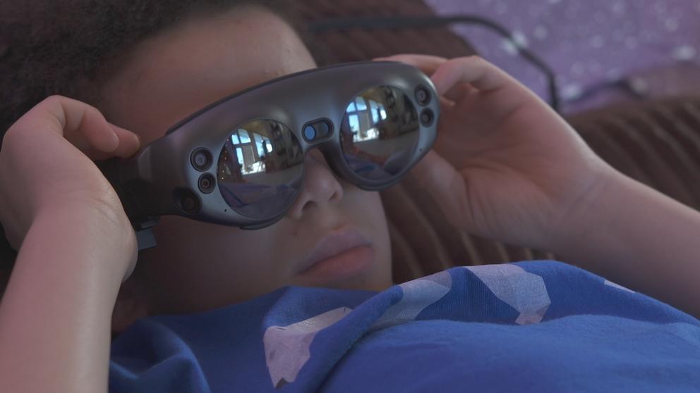 a film still shows a young Black boy lying on his back while wearing VR goggles