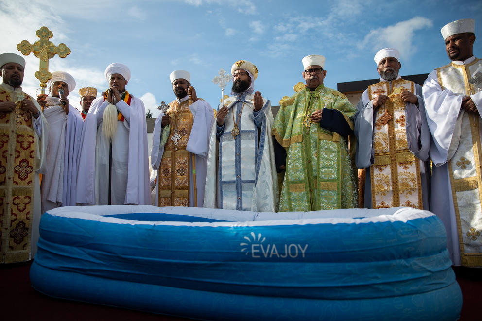 Priests in traditional religious clothes stand around a inflatable pool
