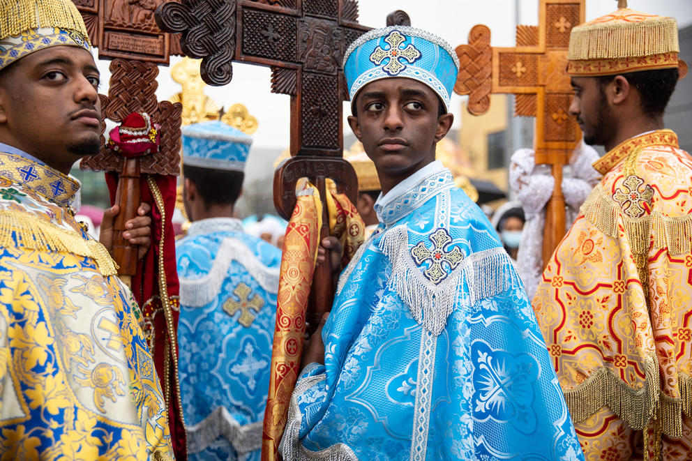 Three young men wearing gold and blue robes hold large wood crosses