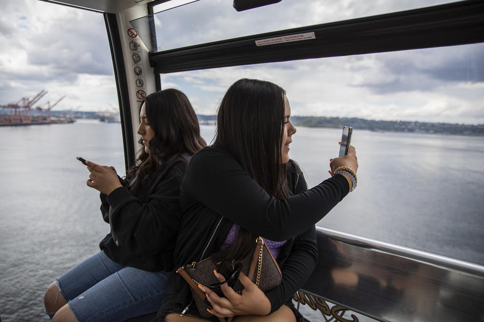 two girls sit in the great wheel looking out toward Elliott Bay