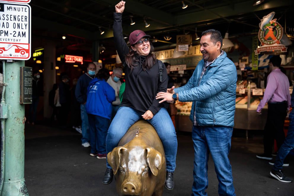 A woman with her arm up sits on a brass pig 