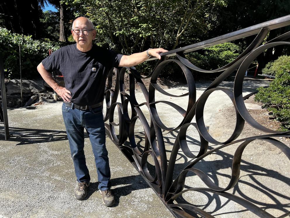 a man wearing jeans and a black t-shirt stands next to an ornamental gate