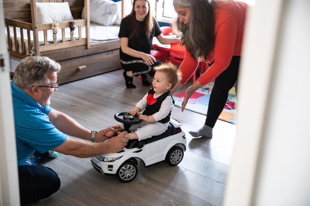 Ten-month-old Max plays with his mother, Olena Roze, and their hosts Irina and John VanPatten in their home.