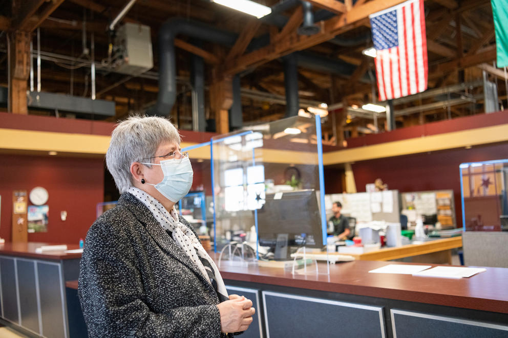 A woman in a face mask stands inside her workplace