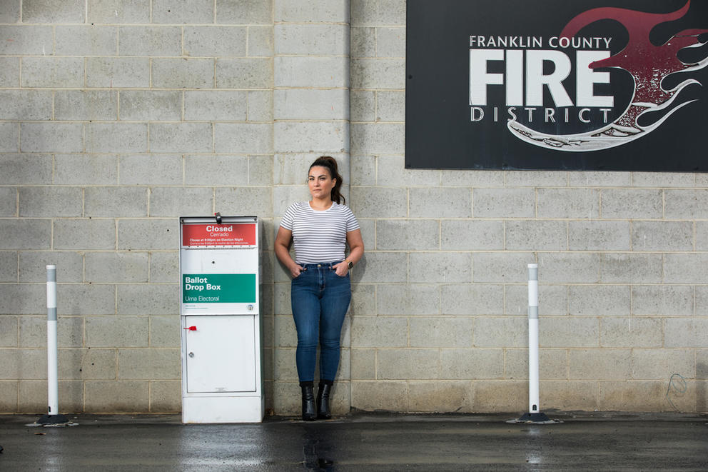 A woman stands next to a ballot box