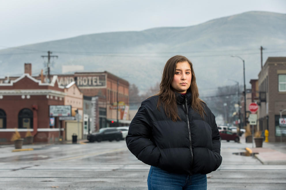 A woman wearing a puffer coat poses for a photo in a town street