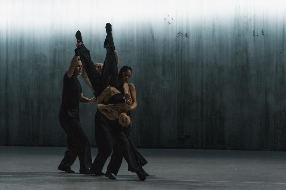 a tight group of dancers, on upside-down and carried by the others, on a dark stage