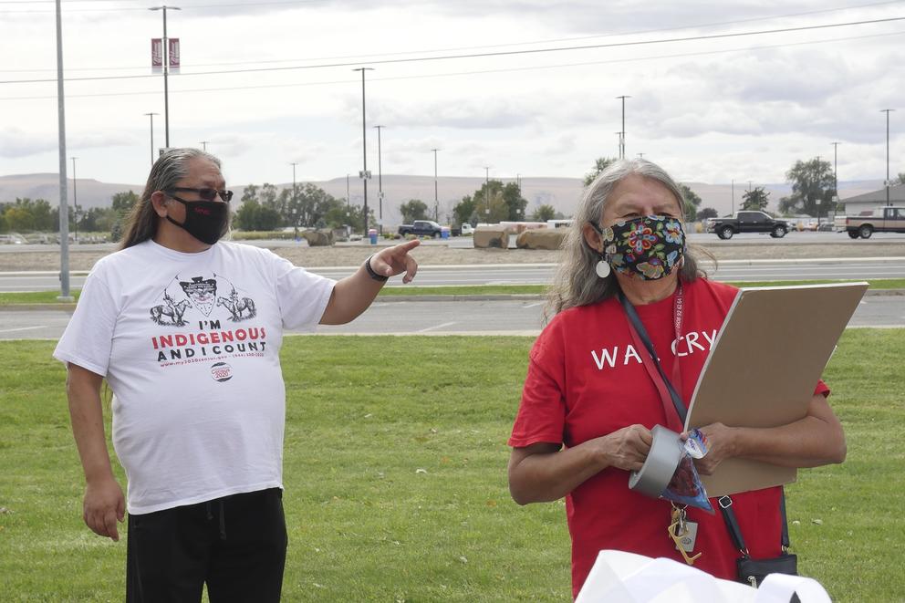 Mathew Tomaskin points while Patricia Whitefoot hold a clipboard in the foreground, outdoors