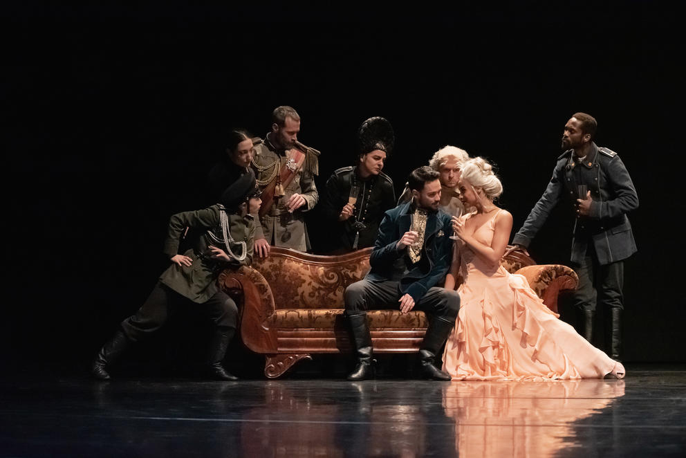 group of actors on stage in 19th century period costume surrounding an antique couch