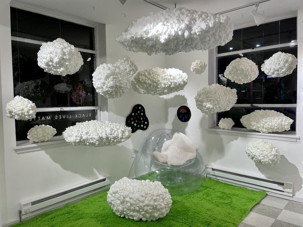 a room in which cottony white cloud sculptures are suspended above a fake green grass rug