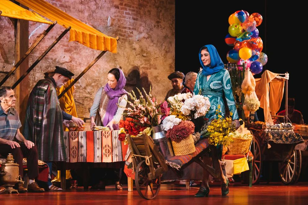 a brightly colored stage set of an Afghan marketplace with smiling shoppers 