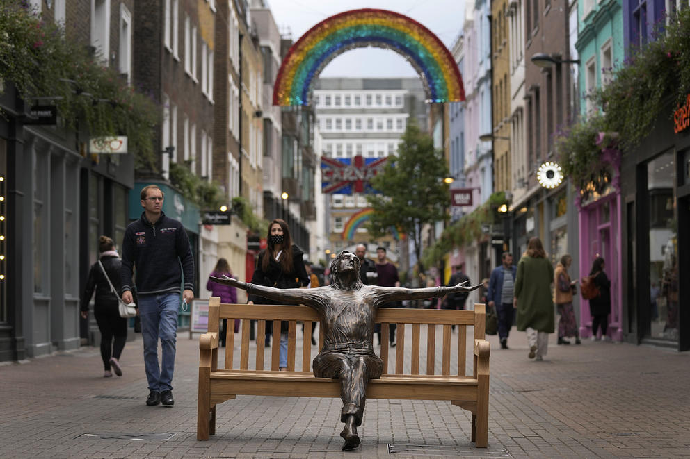 a busy plaza in london with people walking around a bronze statute of john lennon