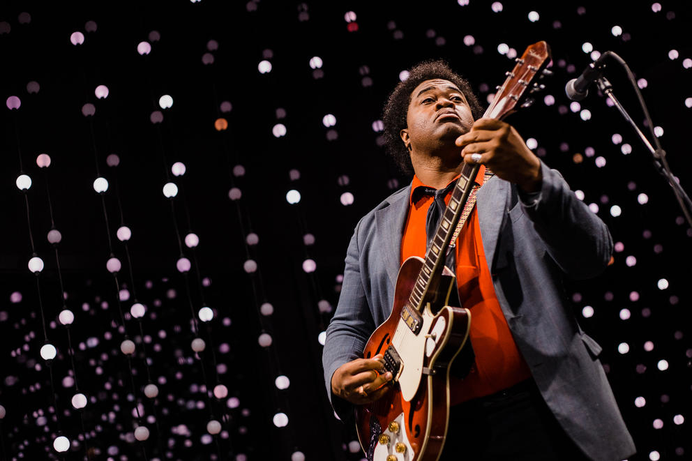 photo of a man playing guitar in a dark room lit with small lights