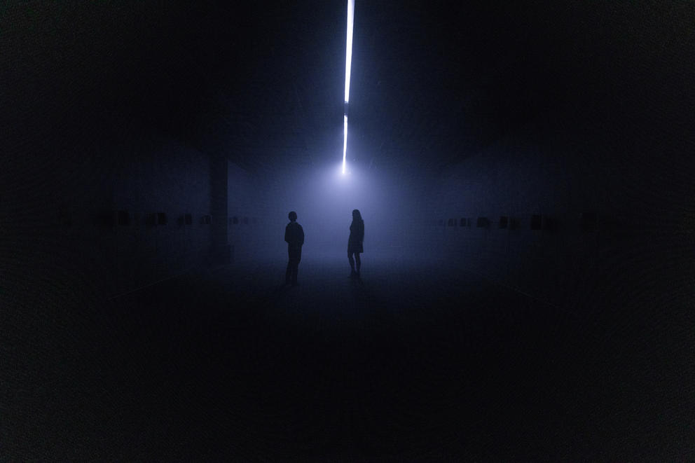 a very dark room with a line of line down the middle and two small human forms way in the distance