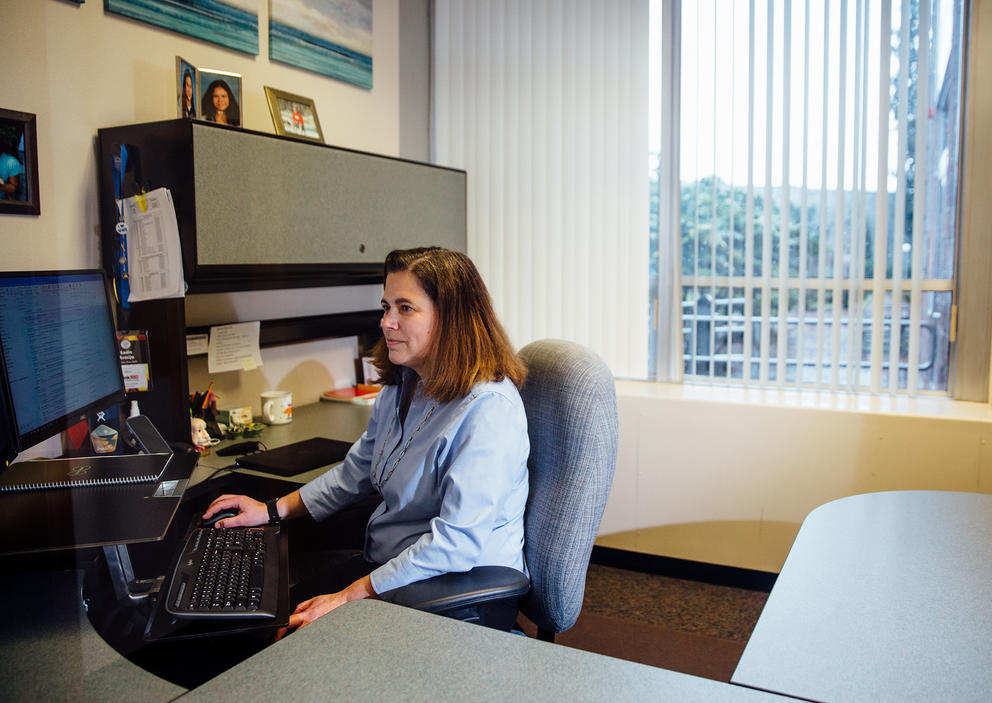 Sadie Armijo sits facing her computer in the corner of her desk with a window behind her.