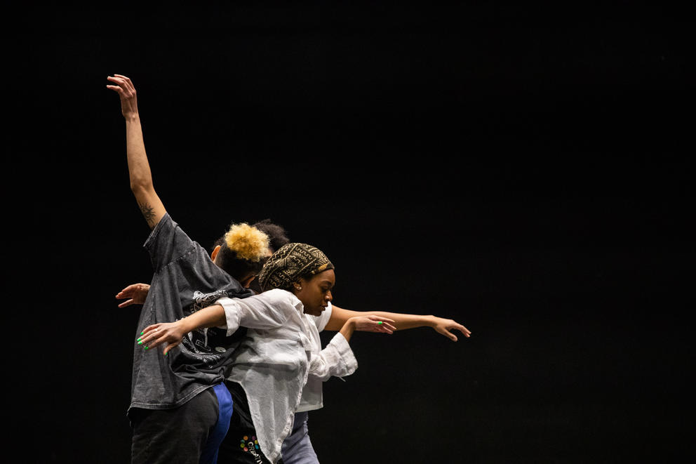 three dancers move, arms extended, on stage