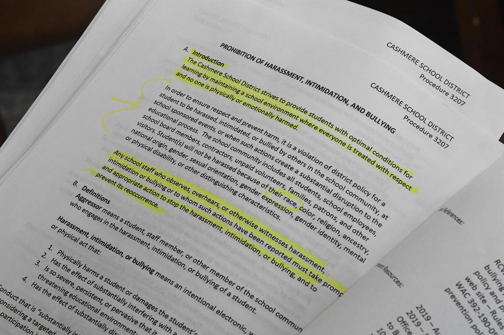 A document on a table with highlighted text lists the Cashmere School District's policies on harassment, intimidation and bullying.