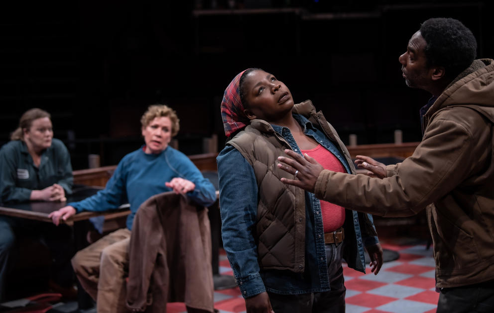 a stage play featuring four characters engaged in an argument, two sitting, two standing