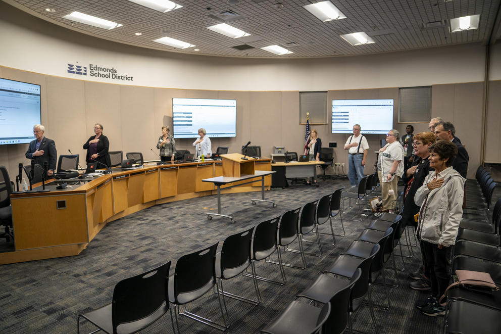 Board members, staff, and members of the public recite the Pledge of Allegiance during an Edmonds School Board meeting.