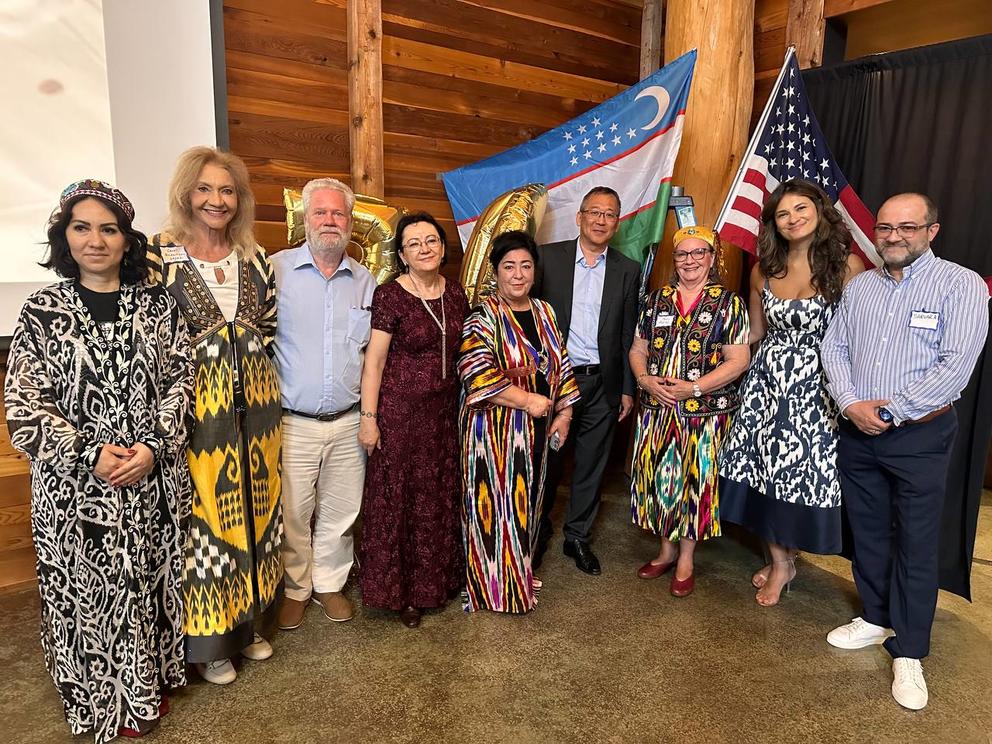 Nine people smile and pose for the camera in front of the flags of Uzbekistan and the United States.