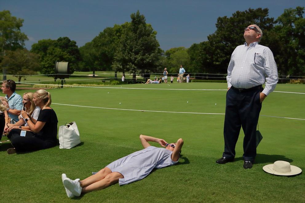 photo of a wide green lawn and a few people wearing eclipse glasses looking up at the sky