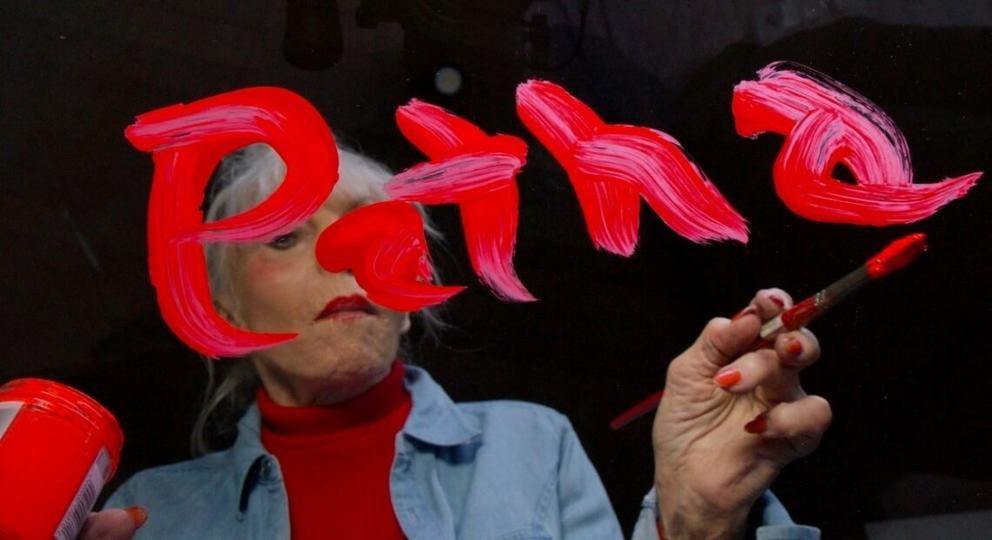 photo of a white haired woman painting the name PATHA in pink on glass