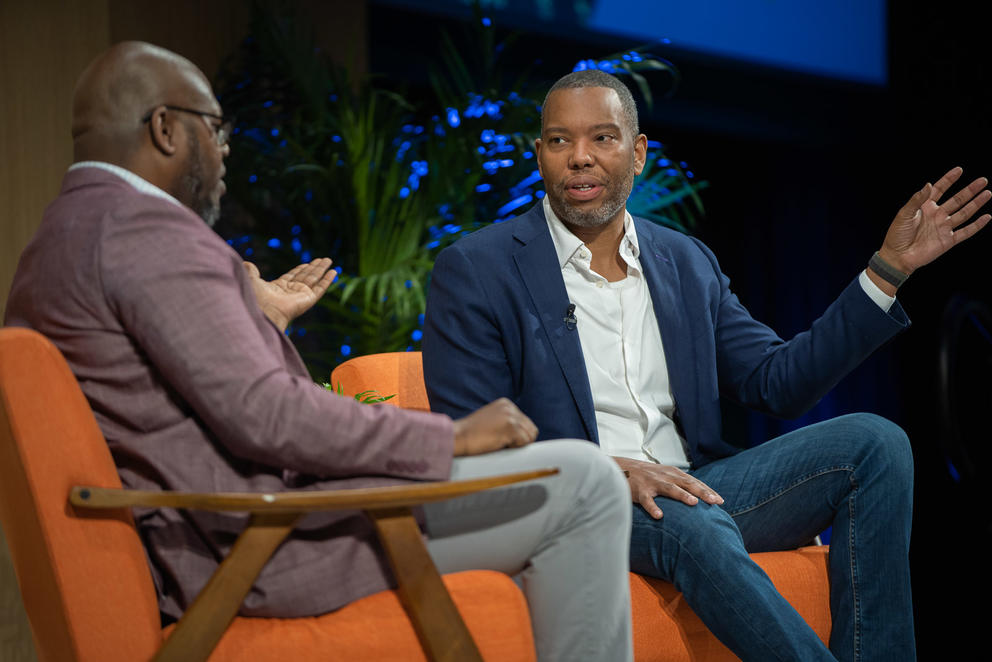 Writer Ta-Nehisi Coates, donning a navy suit, is speaking with Slate's Jason Johnson on stage. 