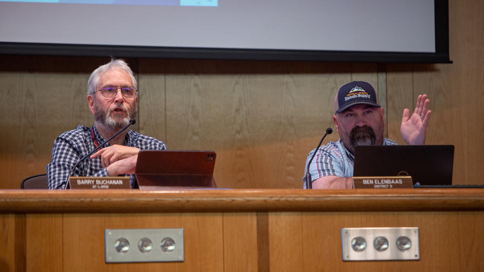 Two County Council members sit behind a wooden desk during a meeting. 