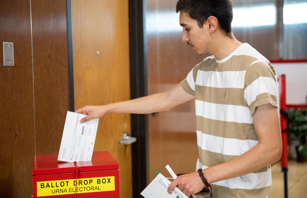 A person deposits a ballot into a box labeled "Ballot Drop Box Urna Electoral" 