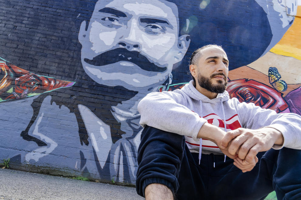 Mural artist Crick Lont (known as dozer_art on social media) is seen next to a commissioned mural he painted, with local graffiti writer Charms, on the exterior of La Esperanza Mercado Y Carniceria in Beacon Hill