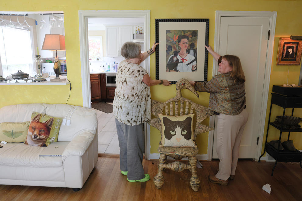 two women hang up a painting in their living room