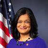 Woman with light brown skin and dark, shoulder-length straight hair wearing a royal blue top and beaded necklace with an American flag and grey background