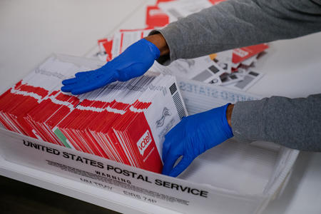 a gloved hand sorts ballots