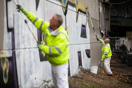 Two men in yellow coats painting over graffiti