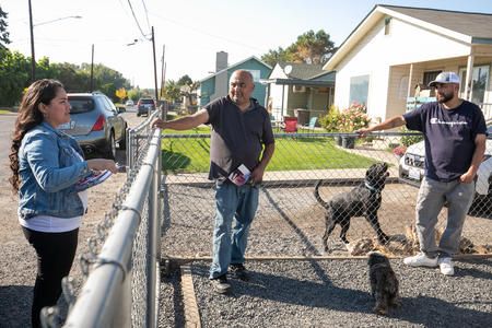 Woman speaking to two men on the other side of a chain-link fence