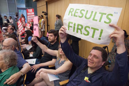 A man at a City Council vote on the business tax holds up a sign advocating for holding off on a new tax until current efforts to reduce homelessness produce more results. (Photo by Matt M. McKnight/Crosscut)