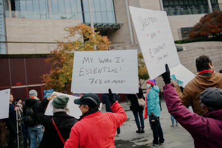 a group of people hold signs at a rally outside seattle city hall