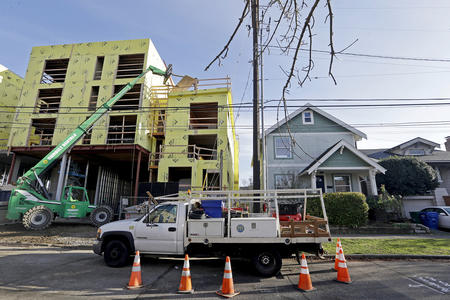 a four story apartment building is under construction next to a single family house. a construction vehicle is in the foreground