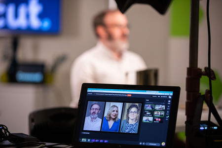 Man in a studio foregrounded by a monitor showing three speakers