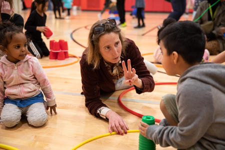 Volunteer Eleanore Mali crouches down to help kids stack cups