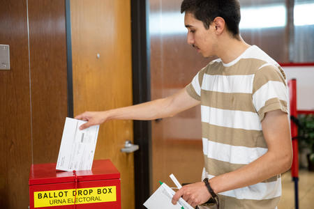 A person deposits a ballot into a box labeled "Ballot Drop Box Urna Electoral" 
