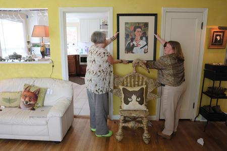 two women hang up a painting in their living room